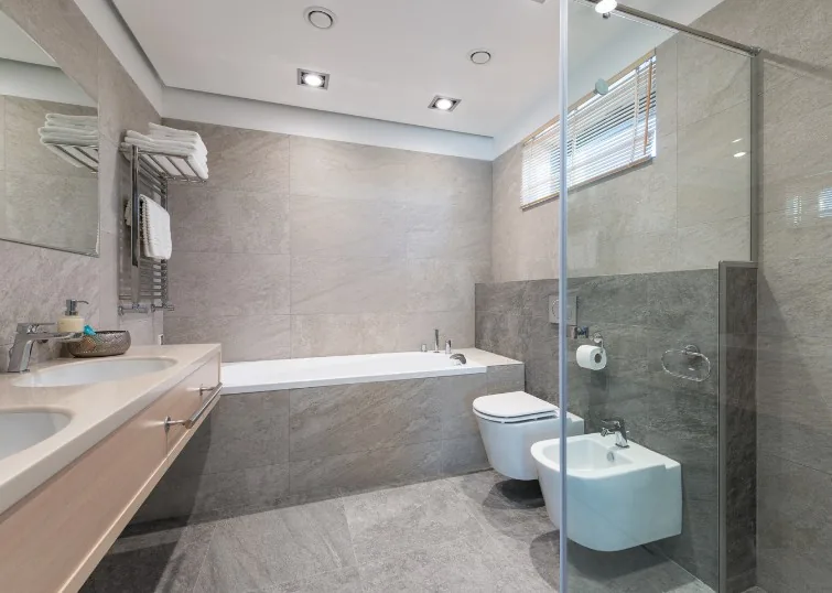 Baño terminado con inodoro y bidé suspendidos, bañera revestida y ducha acristalada en una vivienda de Zuera