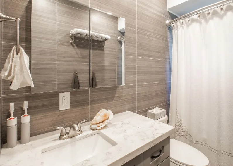 Lavabo sobre encimera de piedra y revestimiento efecto madera gris en un aseo reformado